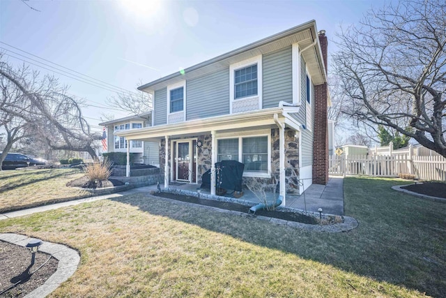 view of front of home featuring a front yard, fence, a porch, a chimney, and stone siding