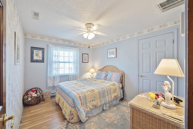 bedroom with visible vents, a textured ceiling, wood finished floors, and a ceiling fan