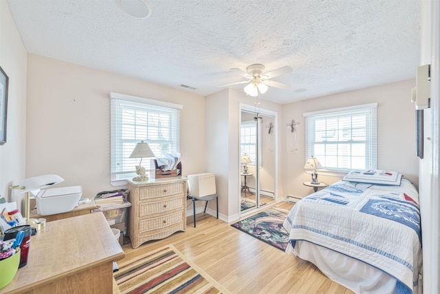 bedroom featuring visible vents, multiple windows, light wood-type flooring, and a baseboard heating unit