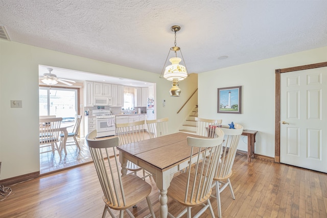 dining area featuring visible vents, a textured ceiling, stairs, and light wood finished floors