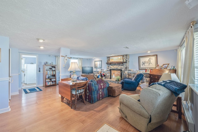 living area with a wealth of natural light, light wood-style flooring, a fireplace, and a textured ceiling