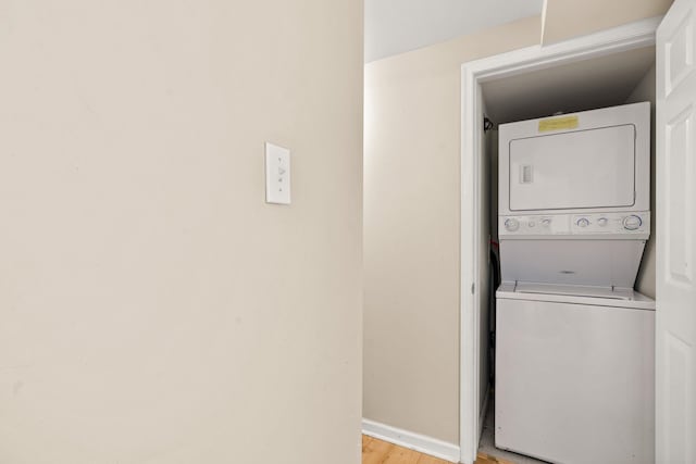 clothes washing area with light wood-type flooring, stacked washer and dryer, baseboards, and laundry area