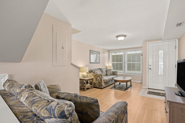 living room featuring electric panel, visible vents, baseboards, and light wood finished floors