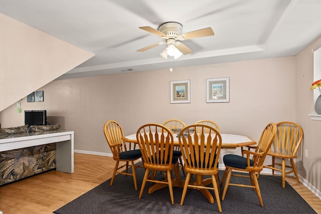 dining room with light wood finished floors, baseboards, a raised ceiling, and a ceiling fan