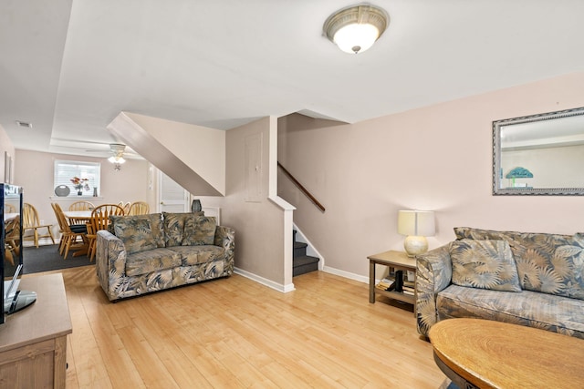 living area with light wood-style flooring, visible vents, a ceiling fan, baseboards, and stairway