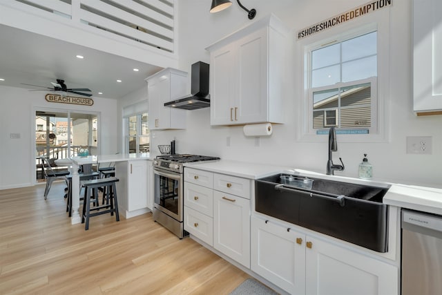 kitchen with wall chimney exhaust hood, stainless steel appliances, white cabinets, recessed lighting, and a ceiling fan