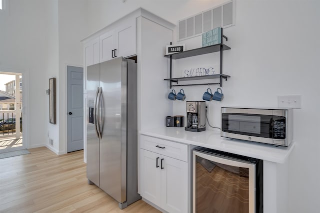 bar featuring stainless steel appliances, light wood-style flooring, visible vents, baseboards, and beverage cooler