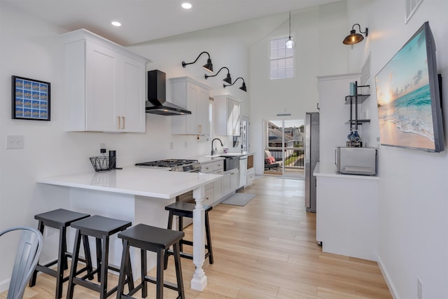 kitchen with a breakfast bar, light wood-style flooring, white cabinets, wall chimney exhaust hood, and appliances with stainless steel finishes