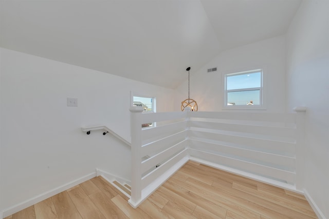 staircase featuring vaulted ceiling, visible vents, baseboards, a notable chandelier, and wood finished floors
