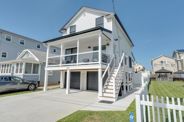 beach home with a front lawn, concrete driveway, an attached garage, a porch, and a gazebo