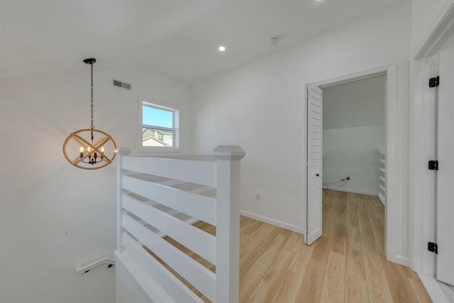 hall featuring lofted ceiling, light wood finished floors, visible vents, an upstairs landing, and a chandelier