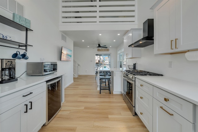 kitchen featuring light wood-style flooring, white cabinetry, wall chimney range hood, beverage cooler, and appliances with stainless steel finishes