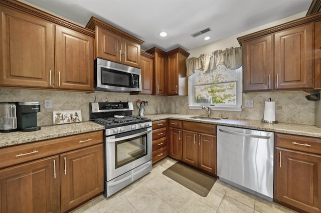 kitchen featuring stainless steel appliances, a sink, light stone counters, and decorative backsplash