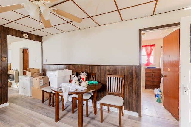 dining room featuring a paneled ceiling, ceiling fan, wood walls, and light wood-type flooring