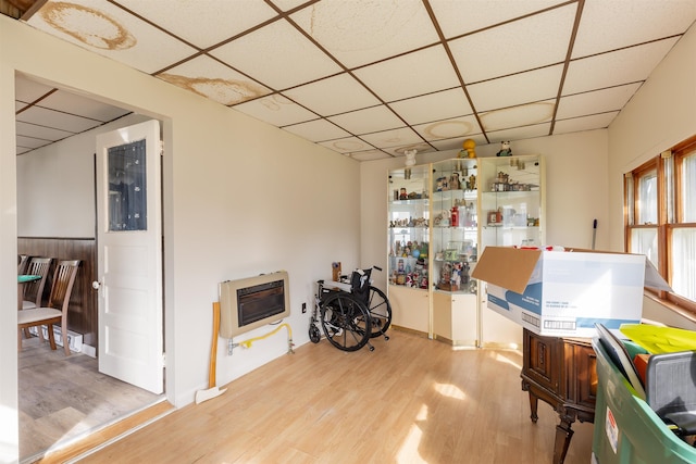 miscellaneous room featuring a paneled ceiling, heating unit, and light hardwood / wood-style flooring