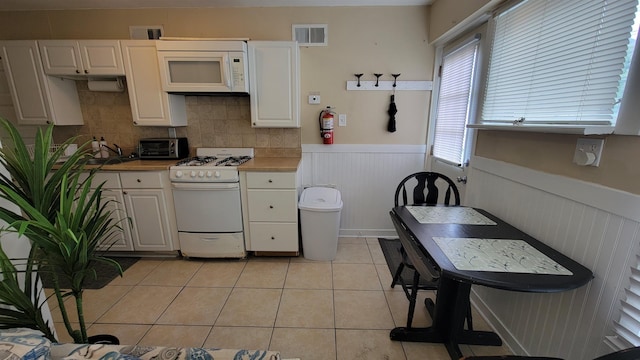 kitchen featuring backsplash, white cabinets, light tile patterned floors, and white appliances