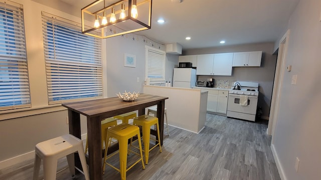 kitchen with white cabinetry, light wood-type flooring, white appliances, and hanging light fixtures