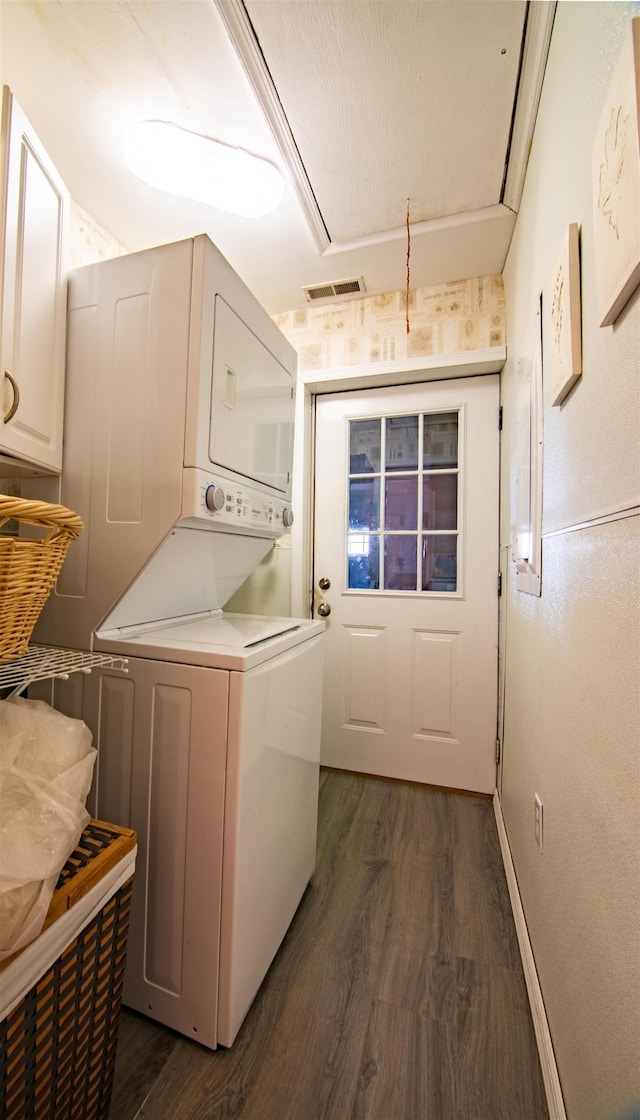 laundry room with stacked washer and dryer, dark wood-type flooring, and cabinets