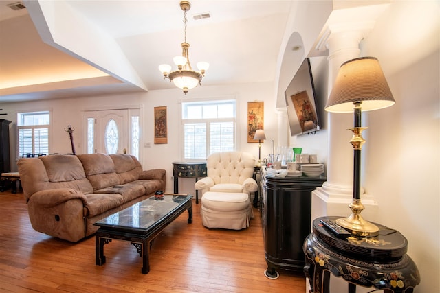 living room with a healthy amount of sunlight, lofted ceiling, hardwood / wood-style floors, and a notable chandelier