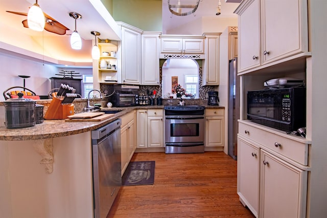 kitchen with appliances with stainless steel finishes, decorative light fixtures, kitchen peninsula, and light hardwood / wood-style flooring