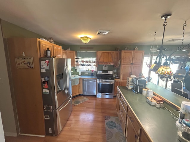 kitchen featuring visible vents, appliances with stainless steel finishes, brown cabinets, light wood-type flooring, and pendant lighting