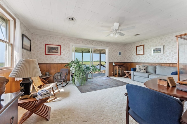 carpeted living room featuring ceiling fan and wood walls