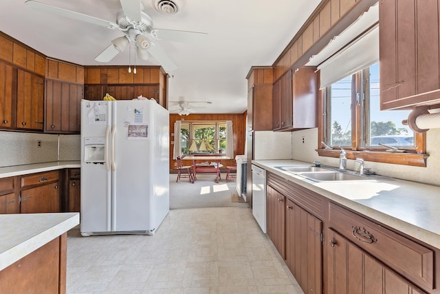 kitchen with white appliances, sink, wooden walls, ceiling fan, and light colored carpet