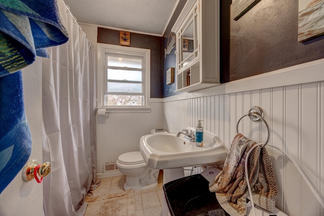 full bathroom featuring toilet, a wainscoted wall, a shower with shower curtain, a sink, and tile patterned floors