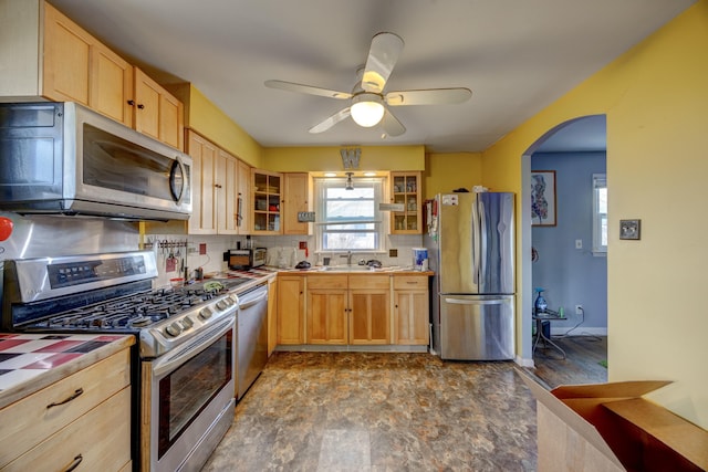 kitchen featuring arched walkways, tile counters, glass insert cabinets, stainless steel appliances, and light brown cabinetry