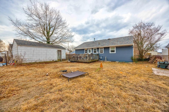 rear view of property featuring a yard, an outdoor structure, a wooden deck, and fence