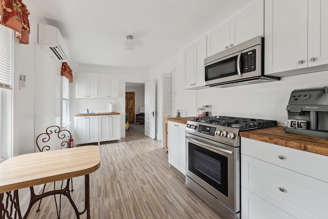 kitchen featuring appliances with stainless steel finishes, light wood-type flooring, white cabinetry, wooden counters, and a wall mounted AC