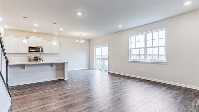 kitchen with stove, dark wood-type flooring, pendant lighting, white cabinetry, and an island with sink