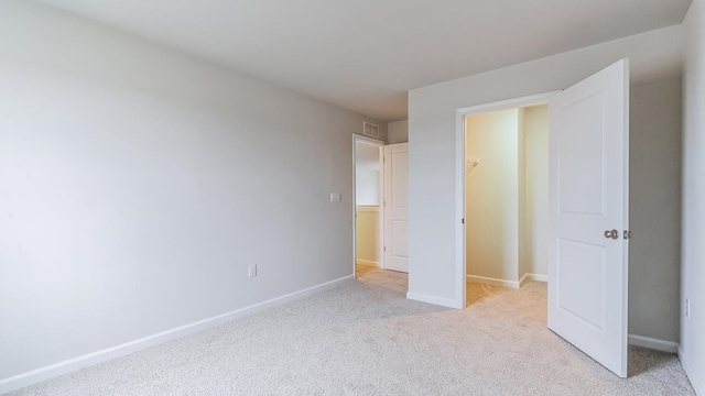 unfurnished bedroom with a walk in closet, light carpet, and a closet