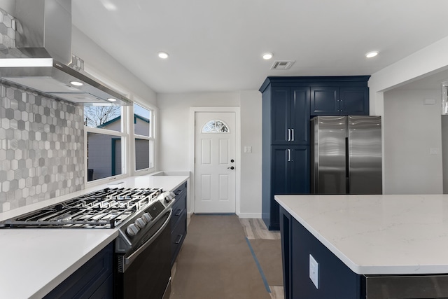 kitchen with blue cabinetry, wall chimney exhaust hood, tasteful backsplash, light stone counters, and appliances with stainless steel finishes