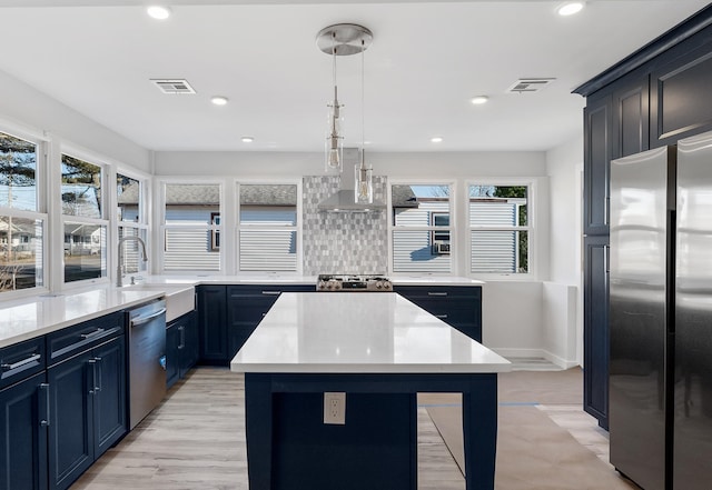 kitchen featuring stainless steel appliances, wall chimney range hood, sink, pendant lighting, and a kitchen island