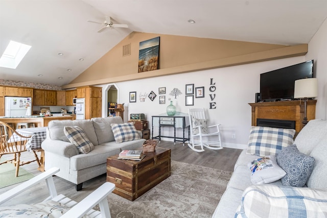 living room with high vaulted ceiling, hardwood / wood-style floors, ceiling fan, and a skylight