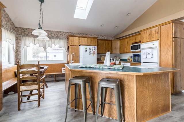 kitchen featuring refrigerator, vaulted ceiling with skylight, stainless steel microwave, decorative light fixtures, and white fridge