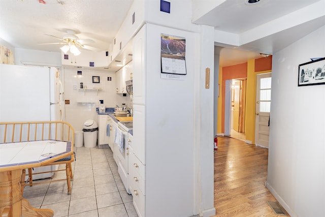 kitchen with ceiling fan, white cabinets, light wood-type flooring, and a textured ceiling