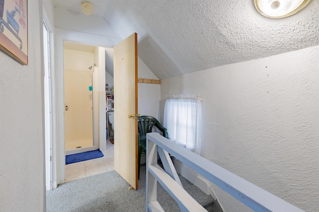 hall with a textured ceiling, lofted ceiling, and light colored carpet