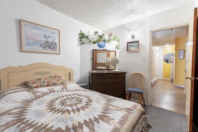 carpeted bedroom featuring a baseboard heating unit and a textured ceiling