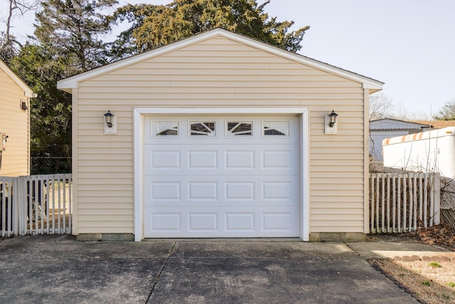 detached garage featuring concrete driveway and fence