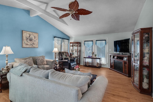 living area with a fireplace, vaulted ceiling with beams, wood finished floors, and ceiling fan