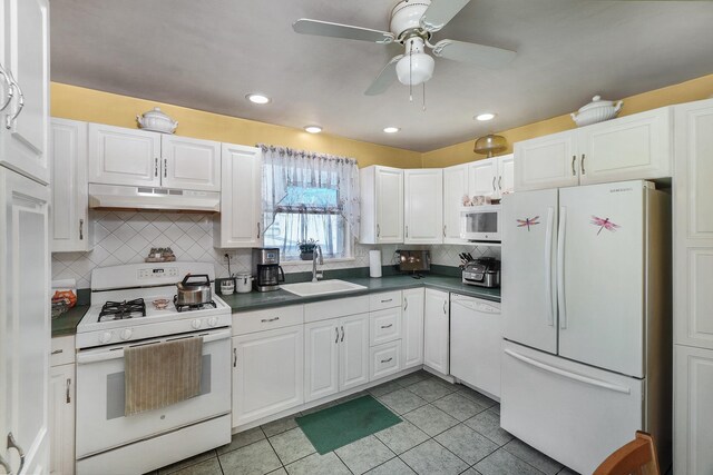 kitchen with a sink, under cabinet range hood, dark countertops, white cabinetry, and white appliances