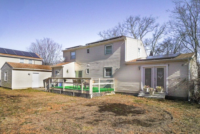 rear view of house featuring a wooden deck, roof mounted solar panels, a lawn, and an outdoor structure