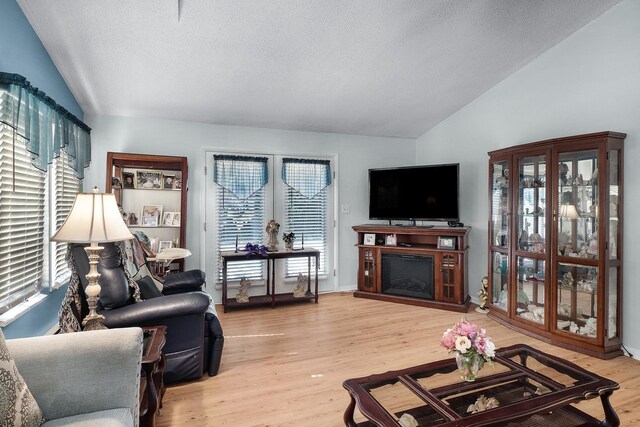 living area featuring a textured ceiling, light wood-style flooring, a fireplace, and vaulted ceiling