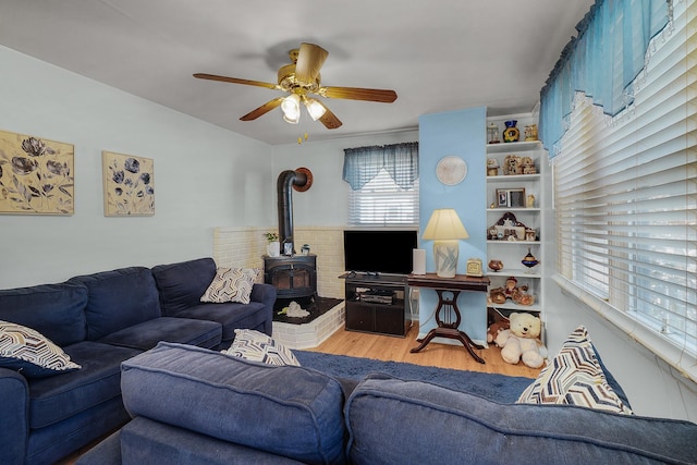 living room featuring a wood stove, a ceiling fan, and wood finished floors