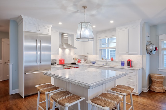 kitchen with wall chimney exhaust hood, stainless steel built in refrigerator, white cabinets, a center island, and hanging light fixtures