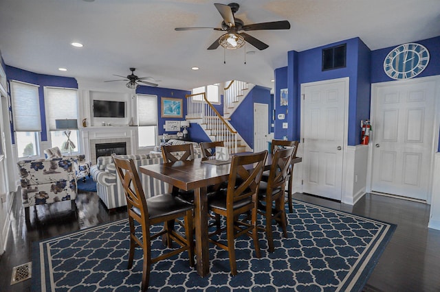 dining area with ceiling fan, a fireplace, and dark wood-type flooring