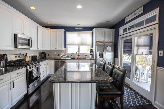 kitchen featuring a center island, stainless steel appliances, dark stone counters, a breakfast bar, and white cabinets