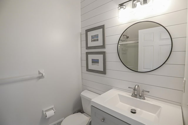 bathroom featuring vanity, toilet, a shower with shower door, and wooden walls